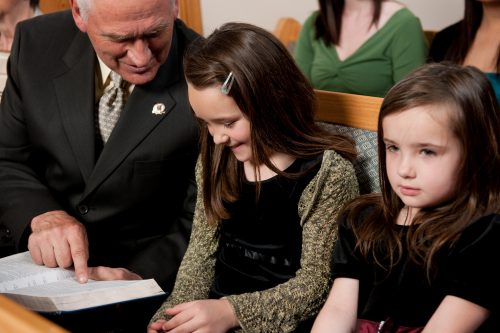 Eldre mann og to barn som sitter sammen i kirken